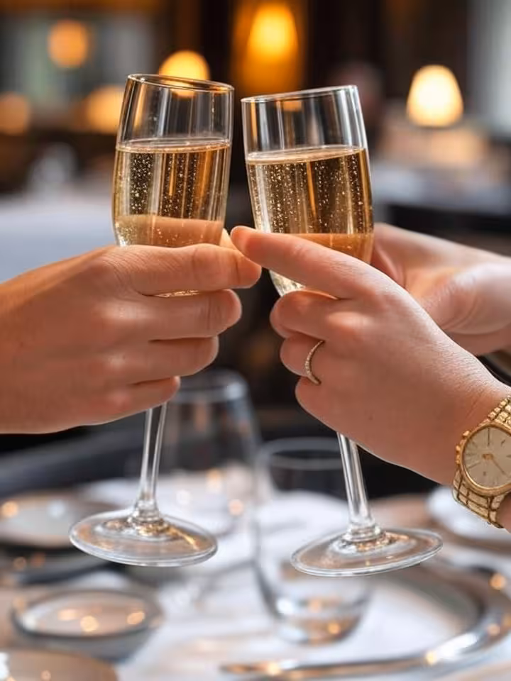 Close-up detail shot of two hands toasting with champagne glasses at an upscale restaurant, one hand